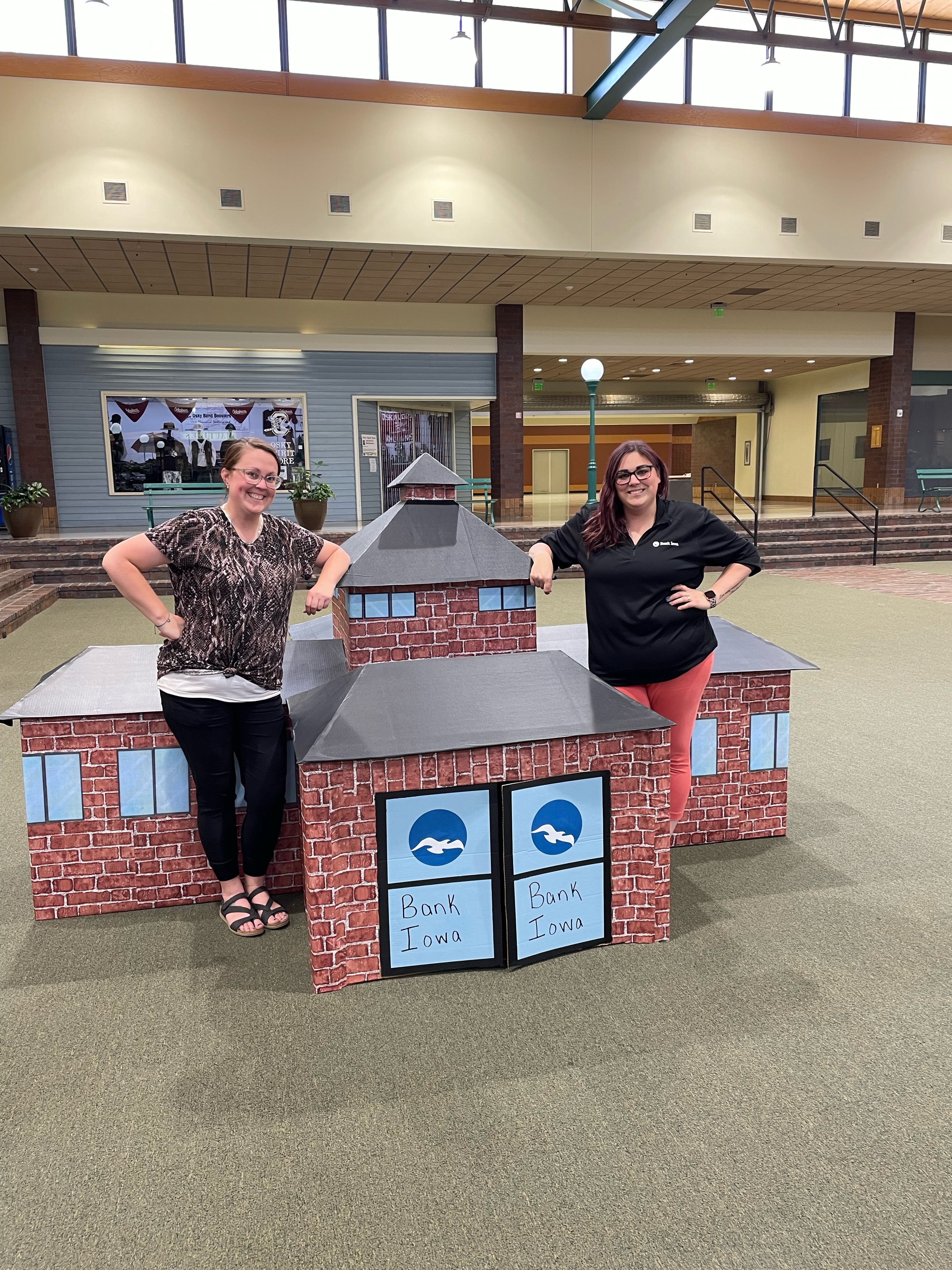 Women standing and smiling with cardboard Bank Iowa rep